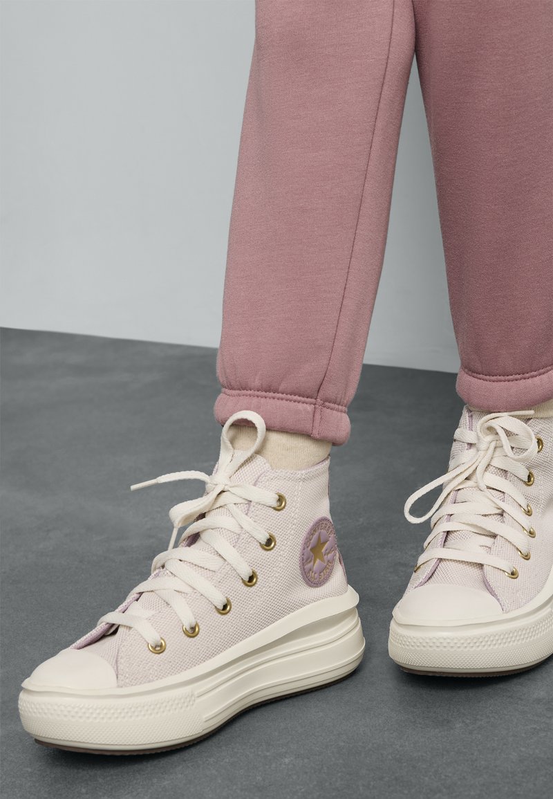 Heledsideme sneakerid heledroosas kangast, millel on kuldsed silmad, valge kummitammi ja külgedele ringikujuline lilla logo.