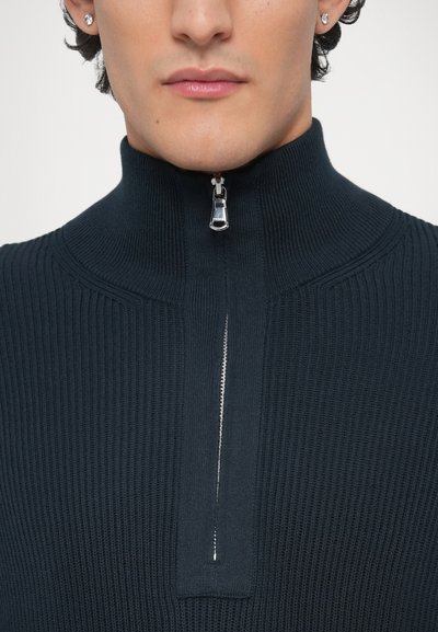 Pull-over côtelé bleu marine avec un col montant et une demi-fermeture éclair. Texture lisse avec une épaisseur modérée, soulignant une coupe ajustée.
