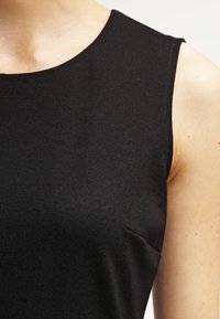 Czarny top bez rękawów wykonany z miękkiego materiału, z okrągłym dekoltem i minimalistycznym designem, posiadający dyskretną kieszeń boczną.