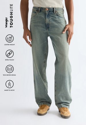 Osoba nosząca luźne, jasnoniebieskie jeansy i beżowe trampki, z tekstem podkreślającym lekkie, wytrzymałe i technologicznie zaawansowane dżinsy stworzone do swobodnego ruchu.