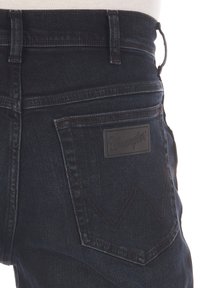 Jeans de mezclilla azul oscuro con un diseño ajustado, que presentan un logo de parche de cuero en el bolsillo trasero y detalles de costura distintivos.