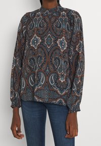 Blouse à manches longues avec un motif paisley en bleu marine, marron et blanc. Col froncé et poignets élastiques. Tissu léger avec un design fluide.