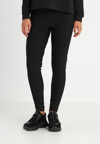 Svart randig leggings i stretchigt material, med en åtsittande design och resårmidja, tillsammans med svarta sneakers.