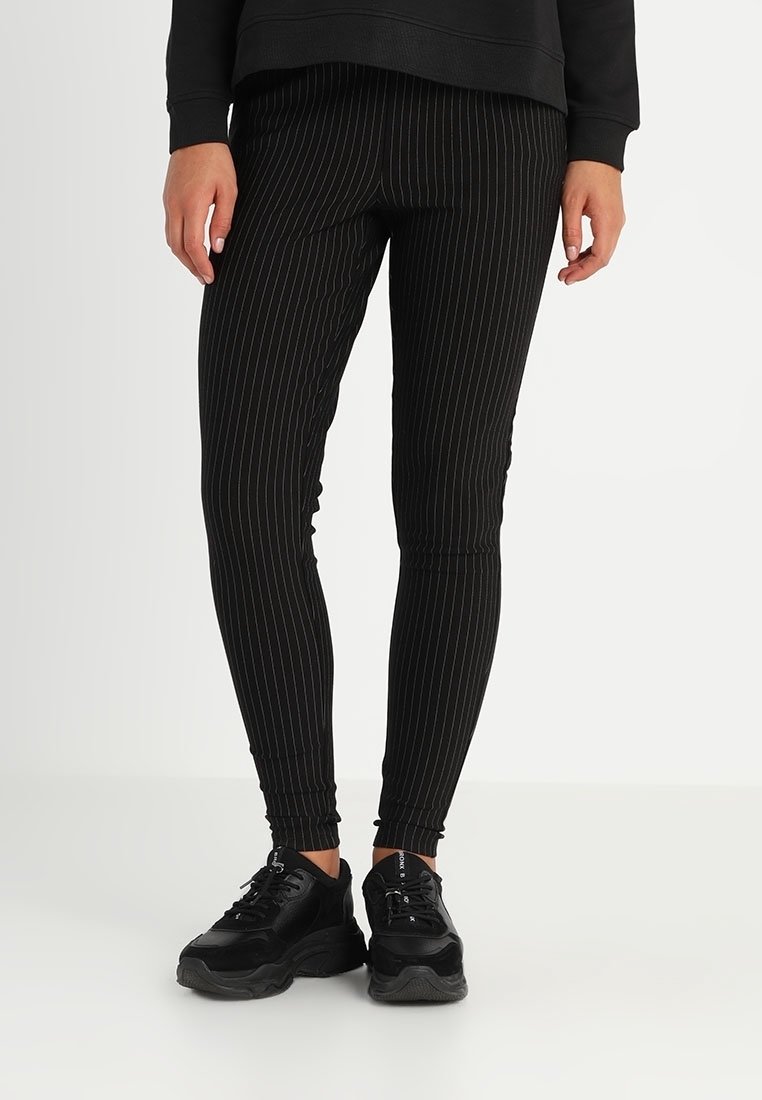 Svart randig leggings i stretchigt material, med en åtsittande design och resårmidja, tillsammans med svarta sneakers.