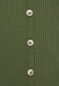 Tessuto a coste verde scuro con una texture verticale; presenta quattro bottoni rotondi di colore chiaro lungo il centro.