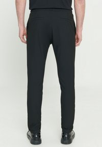 Zwarte slim-fit broek met een soepele textuur, elastische tailleband en twee achterzakken. Draagt zwart schoenen, wat een gestroomlijnd silhouet laat zien.