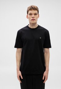 Μαύρο βαμβακερό μπλουζάκι με κοντά μανίκια, στρογγυλή λαιμόκοψη και μικρό λογότυπο στο αριστερό στήθος. Ομαλή υφή και κλασική εφαρμογή.