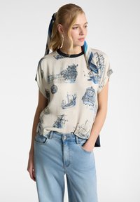 Blusa cremosa a maniche corte con stampa nautica blu, caratterizzata da navi e globi. Progettata con un collo rotondo e una vestibilità rilassata.
