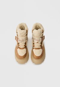 Par de botas de invierno forradas de piel de oveja en color beige y crema, con suelas gruesas y correas de la marca "BUFFALO", vistas desde arriba sobre un fondo blanco.