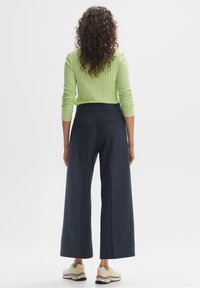 Pantalon large bleu marine en tissu texturé, associé à un haut ajusté en vert citron à côtes. Les chaussures comprennent des baskets de couleur claire.