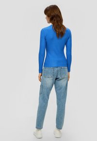 Blauses gestreifter Langarmshirt in Blau, kombiniert mit hellen, baggy Jeans und weißen Plateauschuhen, von hinten betrachtet.