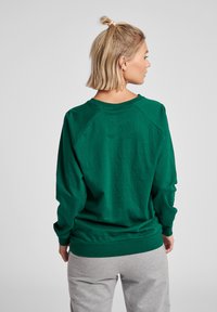 Felpa verde in cotone con vestibilità relaxed, maniche raglan e scollatura rotonda. Tessuto morbido e orlo a costine. Abbinata a pantaloni della tuta grigi.