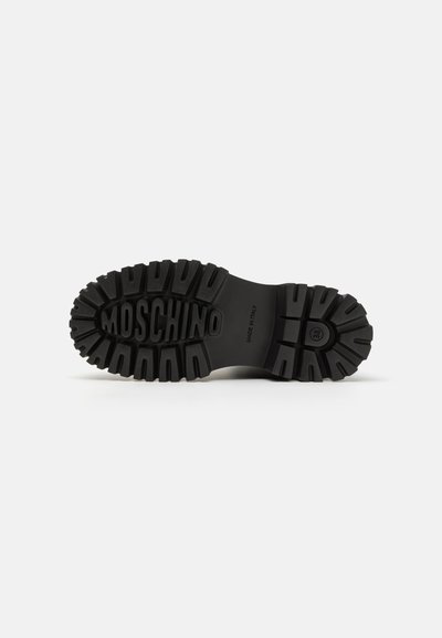 Črna gumijasta podplat čevlja z debelim, strukturiranim profilom, vtisnjenim logotipom "MOSCHINO" in podrobnostjo "MADE IN ITALY".