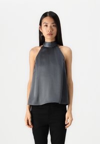 Haut sans manches en halter gris foncé, avec un tissu texturé à finition lisse, un design drapé et un col montant. Associé à un pantalon noir.