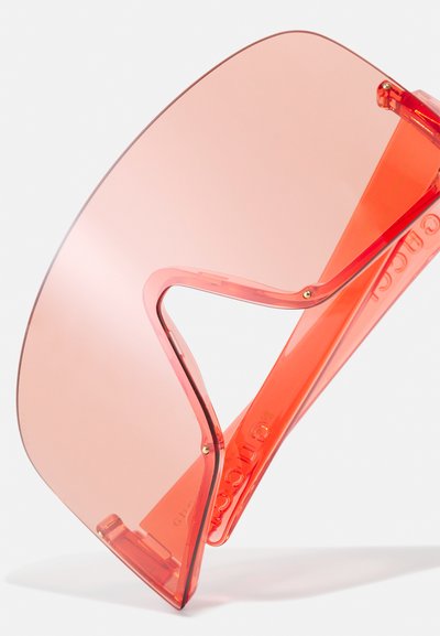 Gafas de sol rojas de gran tamaño con marco de plástico transparente y lentes rosa grandes y curvados; cuentan con una bisagra pivotante para un ajuste ajustable.