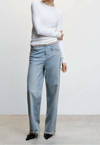 Jasnoniebieskie dżinsy z wysokim stanem o luźnym kroju, z postrzępionymi brzegami, w zestawieniu z białą bluzką z długim rękawem i czarnymi butami na szpilce.