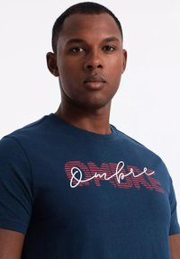 Navy blue cotton t-shirt featuring a red and white graphic text "Ombre" with horizontal stripes. Short sleeves and crew neck design.
