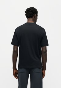 Μαύρο βαμβακερό T-shirt με κοντά μανίκια και στρογγυλή λαιμόκοψη. Λείο ύφασμα, άνετη εφαρμογή. Ορατές λεπτομέρειες ραφών στο τελείωμα.