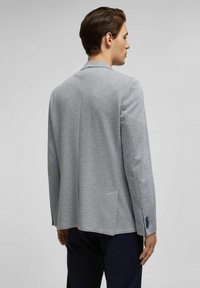 Grauer Strickblazer mit einem strukturierten Kragen, zwei Rückenschlitzen und einem Knopf am Ärmel, entworfen im lässig maßgeschneiderten Stil.