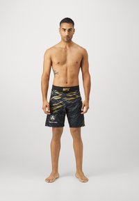 UFC uimar Shorts musta ja kultainen matalavyötäröinen, jossa on aalto-kuvio ja logo vasemmassa lahkeessa. Pintamateriaali on sileä, valmistettu kevyestä materiaalista.