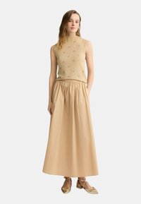 Top senza maniche lavorato a maglia beige con motivo a logo in rilievo, abbinato a una gonna leggera beige fluttuante con vita elasticizzata e tasche.