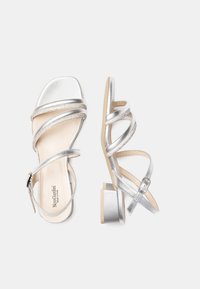 Sandales à talon argenté avec un design à lanières, featuring des lanières métalliques texturées, une semelle douce et un talon bloc rectangulaire.