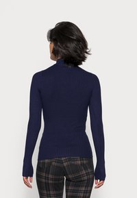 Maglione a collo alto a coste blu navy con maniche lunghe, caratterizzato da una vestibilità aderente e fori per il pollice, abbinato a pantaloni a quadri.