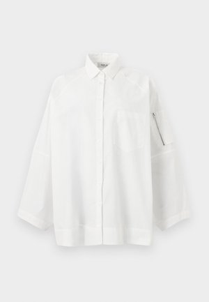 Chemise blanche surdimensionnée à boutons avec col, poche sur la poitrine gauche et poche zippée sur la manche gauche, sur un fond uni.