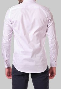 Chemise blanche à manches longues avec une texture lisse, coupe ajustée, couture de dos, et poignets boutonnés. Présente un ourlet arrondi et sans motifs.