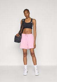 Fekete sportmelltartó, rózsaszín zsinóros rövidnadrág, fehér középmagasságú zoknik és fehér sportcipők. Fekete válltáska pánttal. Egyszerű, sportos megjelenés.