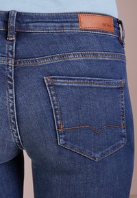 Blå denimjeans har en figurnära design, med kontrasterande orange sömmar, en läder BOSS-logga på midjebandet och en detalj på bakfickan.