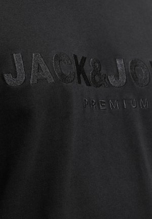 Crna pamučna majica s povišenim, crnim vezivnim tekstom "JACK&JONES PREMIUM." Glatka tekstura i prilagođeni dizajn.
