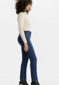 Top de manga larga de canalé en crema claro combinado con jeans rectos de pierna oscura. Los jeans presentan un clásico pespunte en los bolsillos traseros y un ajuste ceñido.
