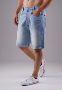 Light blue denim shorts with a faded finish, belt loops, and two front pockets; styled with white sneakers.
