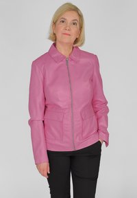 Roze leren jack met een kraag, ritssluiting aan de voorkant en twee voorzakken. Gladde textuur en een getailleerd ontwerp. Zwarte broeken eronder.
