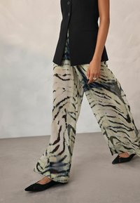 Pantalons large en tissu transparent et léger présentant un motif zébré beige et noir. Associés à un gilet noir ajusté et des ballerines.