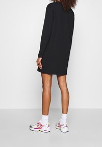 Vestido negro de manga larga con un corte relajado, combinado con zapatillas New Balance coloridas que presentan acentos rosas y una puntera plateada.