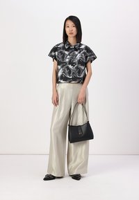 Camicia a righe in bianco e nero tagliata, pantaloni beige chiaro a gamba larga, borsa nera, scarpe basse nere con decorazioni, texture lisce.