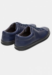 Ett par marinblå läder sko med snörning för fritidsbruk med svarta gummisålar, visade från baksidan på en ljus bakgrund.