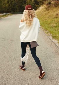 Biela oversized mikina, námornícke legíny a hnedé topánky so ponožkami. Výrazný strapcový detail na mikine a pruhovaný doplnok na legínach.