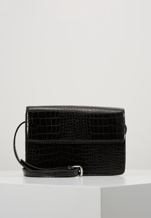 Černá kožená crossbody taška s krokodýlím vzorem, se zapínáním na klopu a nastavitelným popruhem, vystavená na bílém povrchu.