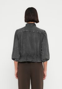 Γκρι τζιν μπουφάν με σφηκοφωλιά στη μέση, φουσκωτά μανίκια και γιακά. Το ύφασμα έχει μαλακή υφή και διακριτικές λεπτομέρειες ξεθωριάσματος.