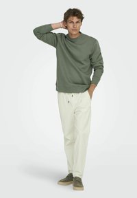 Sweatshirt vert olive avec un col rond et des poignets côtelés, associé à un pantalon écru à cordon de serrage et des baskets vert olive.