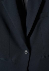 Blazer bleu marine avec un revers cranté, une fermeture à un bouton et deux poches latérales. Tissu lisse avec un léger éclat.