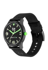 Black watch with a fabric strap, green accents, and a black dial. Features large white numerals, luminous hands, and a round case.