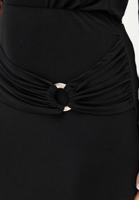Czarna sukienka z zawiązanym detalem z tkaniny w talii i metalicznym okrągłym akcentem, tworzącym efekt marszczenia. Miękka, gładka tekstura.