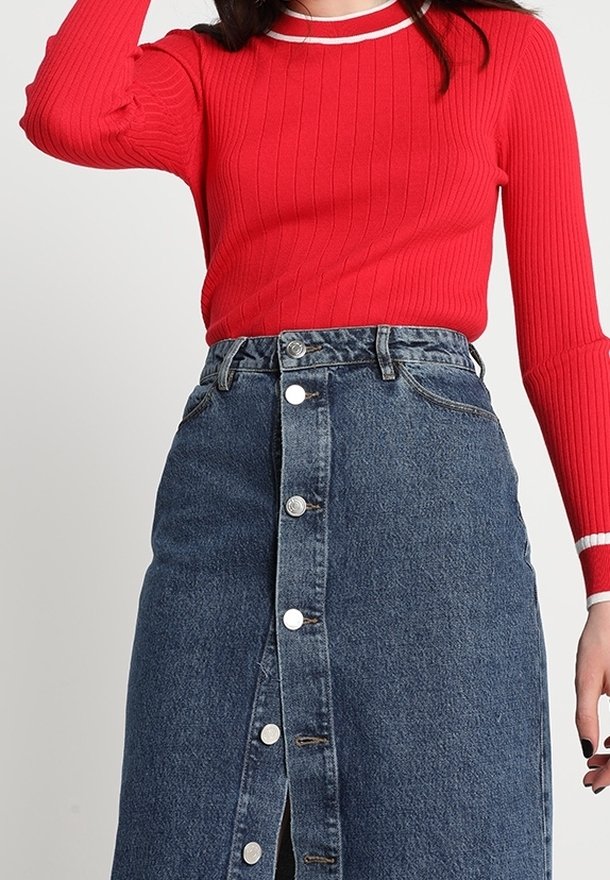 Haut rouge à côtes avec des manches longues et un col rond blanc, associé à une jupe en denim bleu arrivant au genou avec une fermeture à boutons sur le devant et des poches.