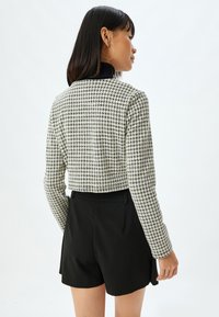 Gekürzter schwarz-weißer Hahnentrittmuster-Pullover mit langen Ärmeln und hohem Kragen, kombiniert mit schwarzen maßgeschneiderten Shorts.