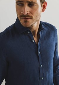 Navyblauwe linnen shirt met een klassieke kraag, knoopsluiting vooraan en lichtgekleurde knopen. Het heeft een gestructureerde stof en een losse pasvorm.