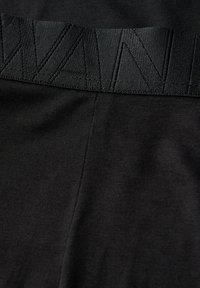 Schwarze Leggings mit einem strukturierten Bund mit erhabenem Muster. Der Stoff ist glatt und dehnbar und bietet Komfort und Passform.